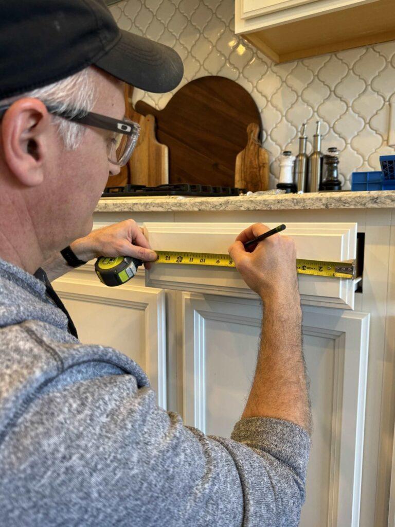 A man measuring a drawer before installing cabinet hardware. 