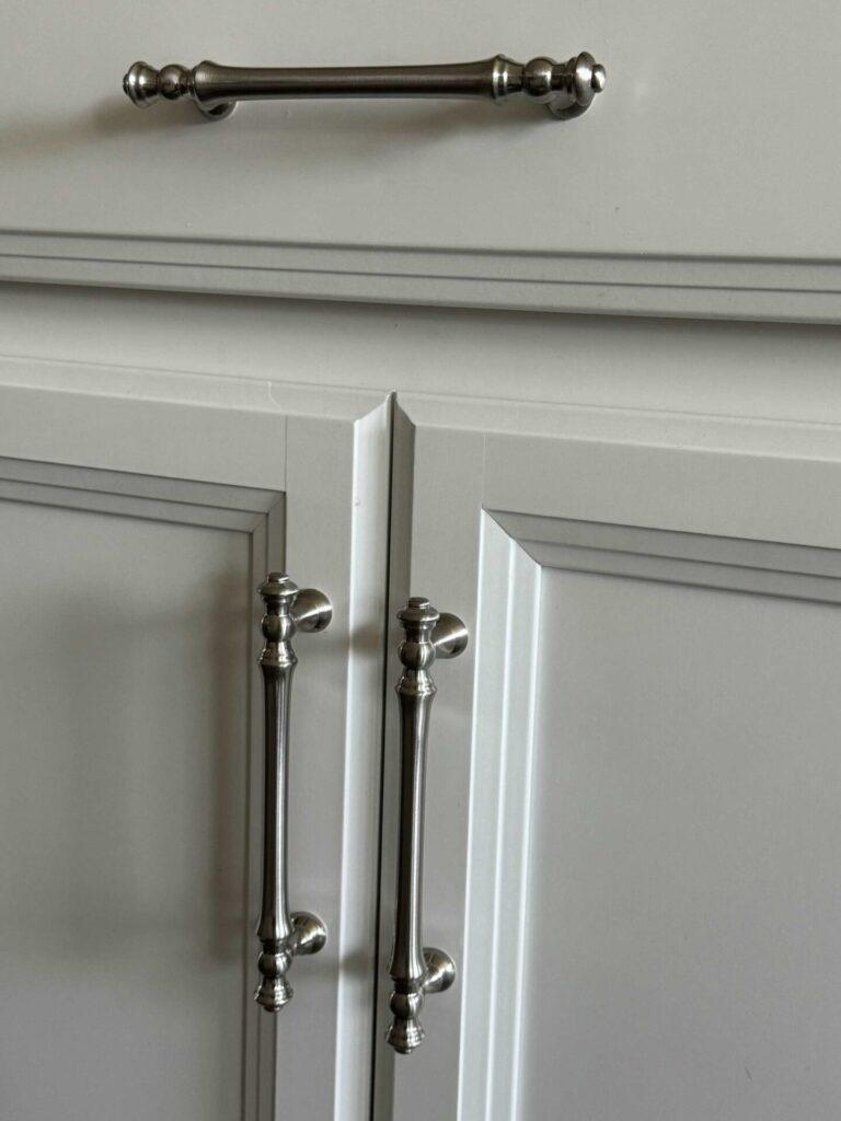 Silver hardware on a white kitchen cabinet and drawer. 