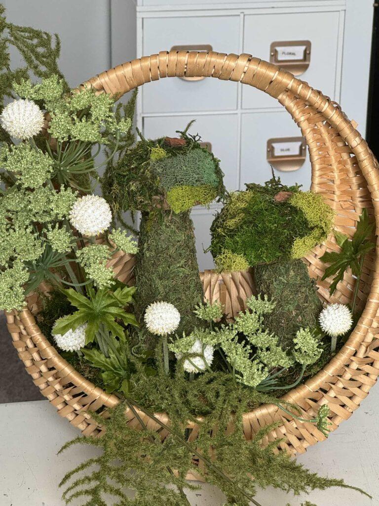 Step five to make a moss mushroom wreath is to add florals and pods to the basket.  