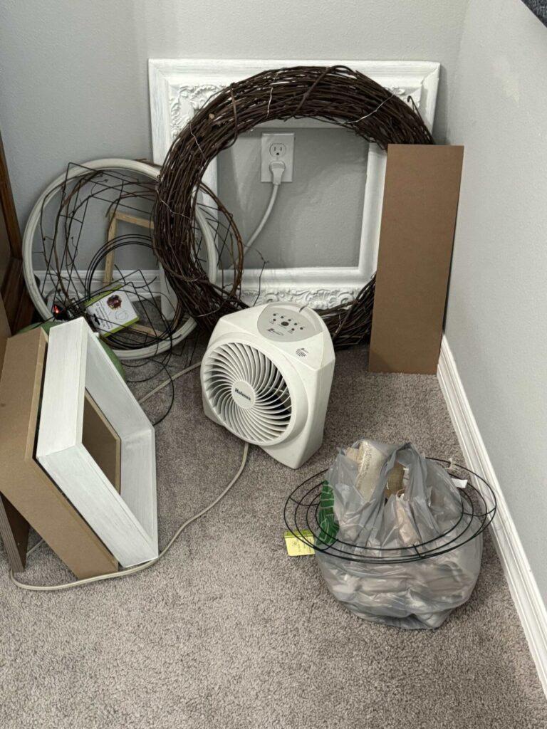 A messy corner filled with wreaths, frames, and a heater. 