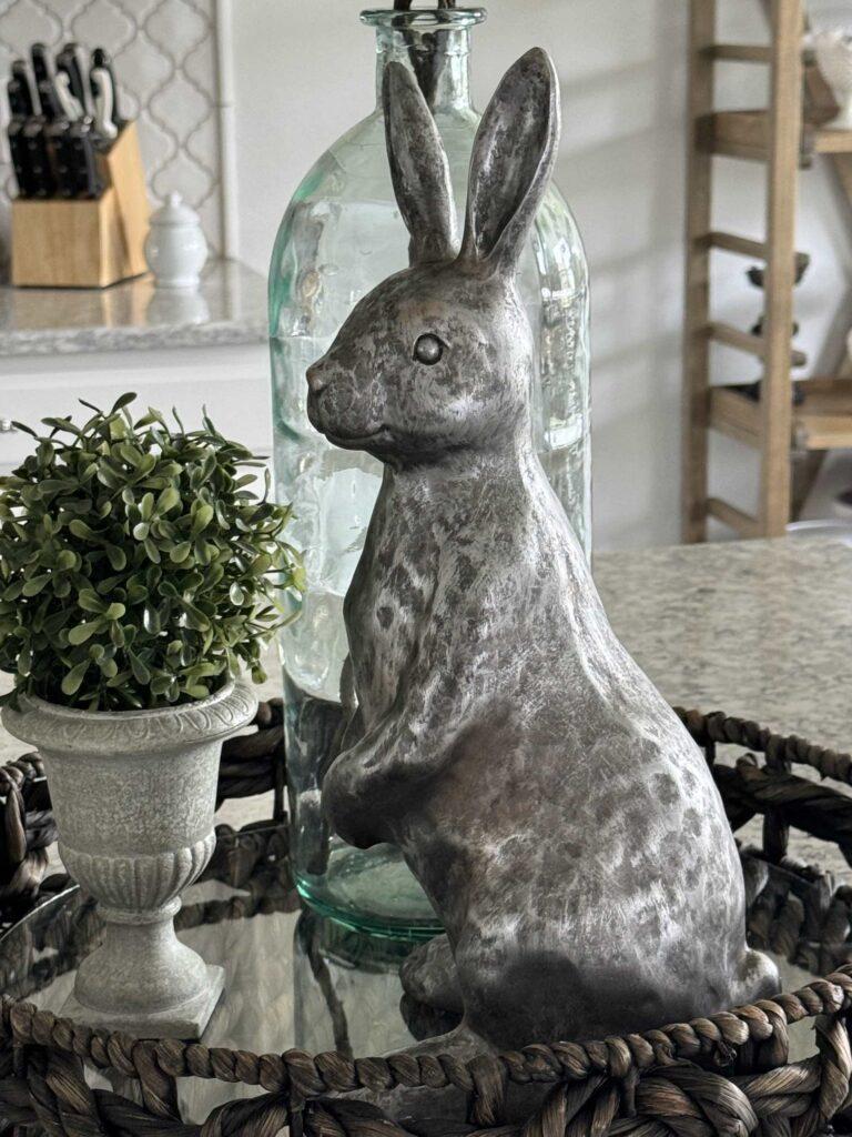 A silver bunny next to a topiary. 