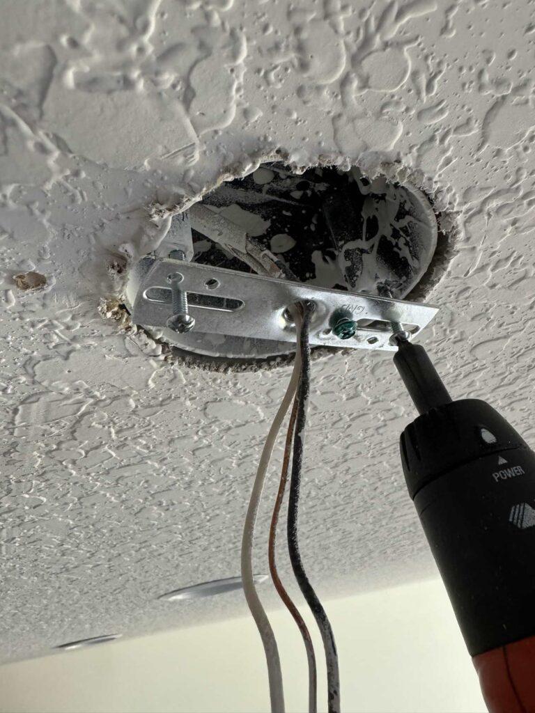 Ceiling bracket being screwed into ceiling fixture. 