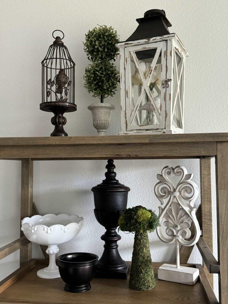 A pie shelf decorated with brown and white dishes, a topiary, a moss mushroom, and a lantern. 