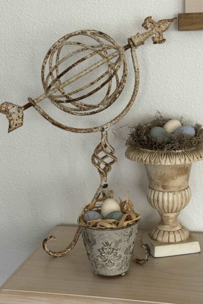 Metal garden statue, an urn, and a metal cup filled with bird's nest and eggs.