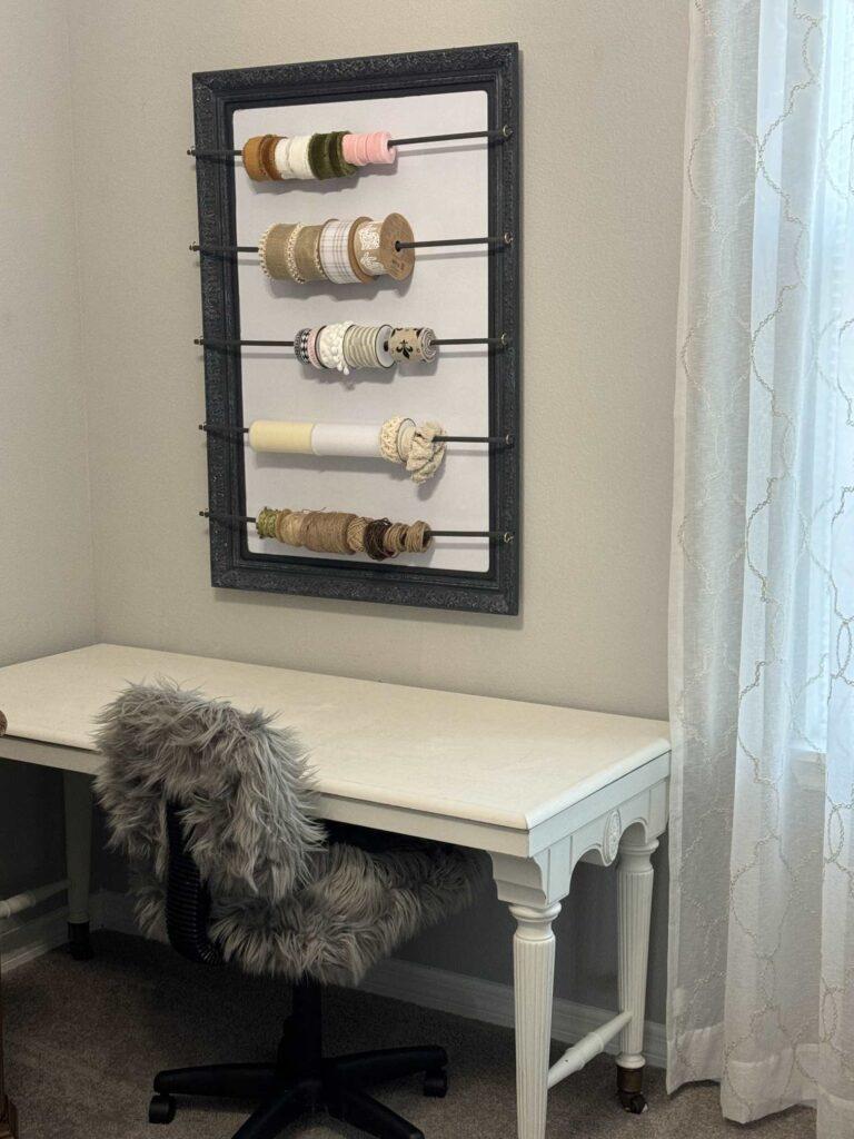 White desk with a frame storing ribbon hanging over it. 