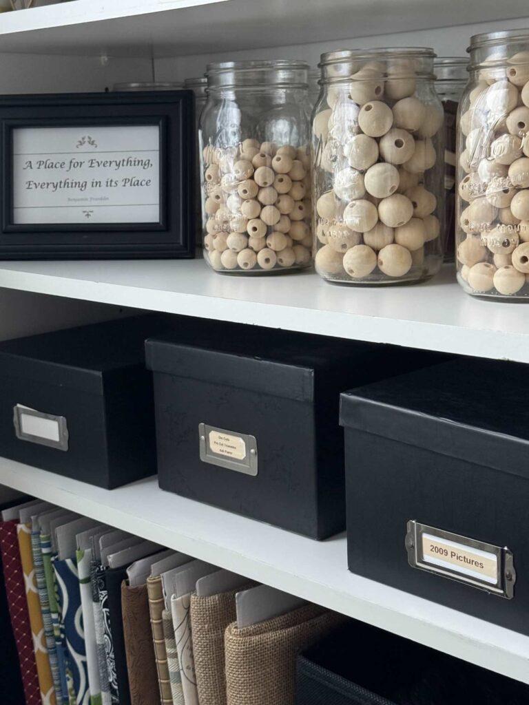 Bookshelves holding wood beads in mason jars and black photo boxes. 