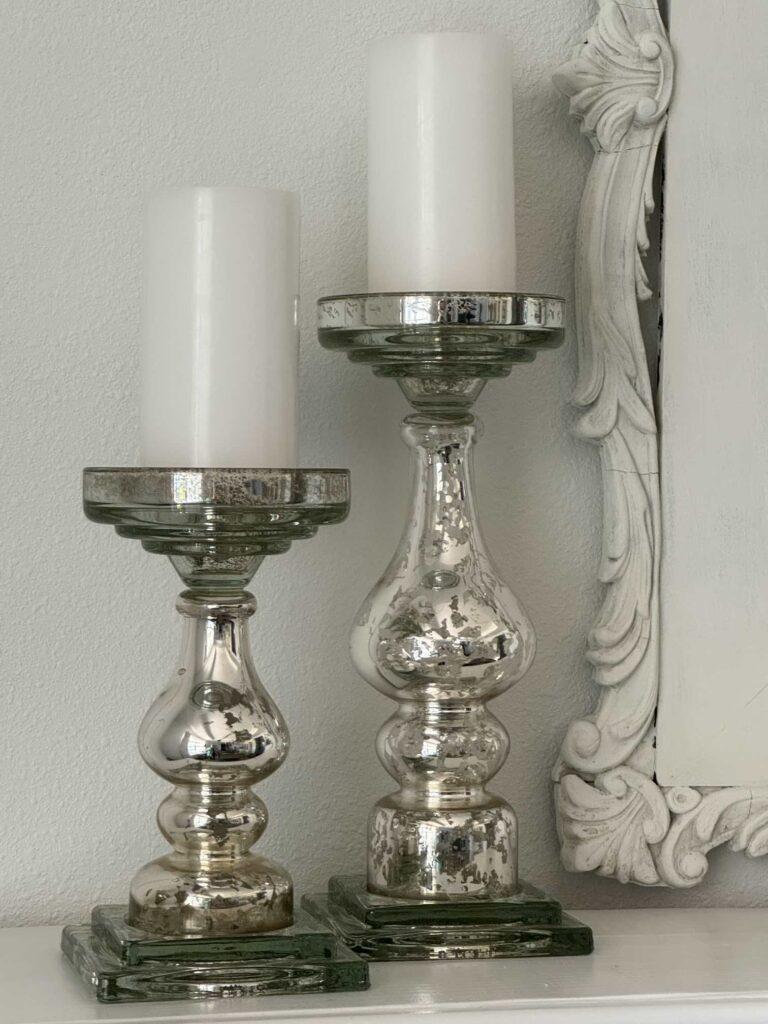 Two mercury glass candlestick holders with white pillar candles. 