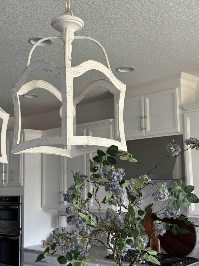 A white pendant light hanging above lilac branches in a kitchen. 