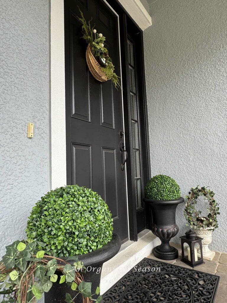 A front door with wreath and surrounded by planters and two lanterns. 