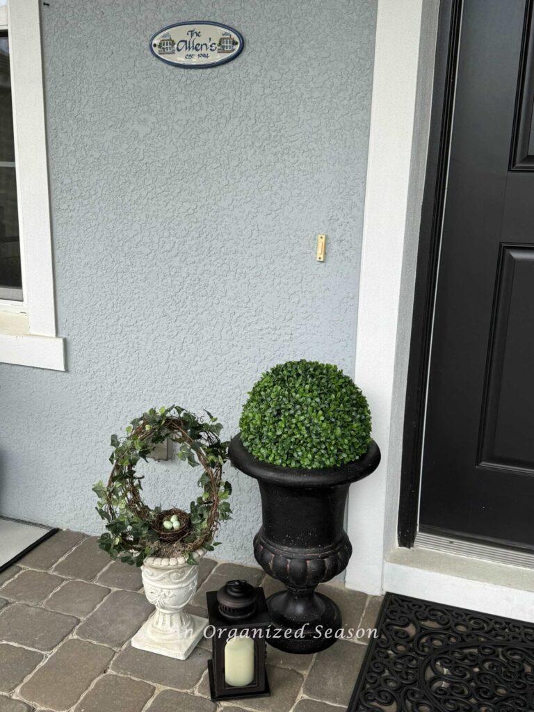 Two planters with faux topiaries and a lantern sitting on a front porch. 