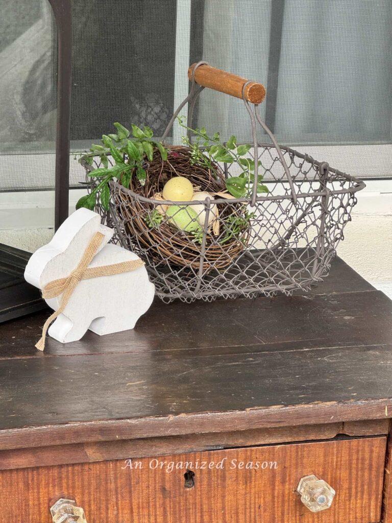 A chicken wire basket with a bird nest inside and a wood bunny sitting next to it.
