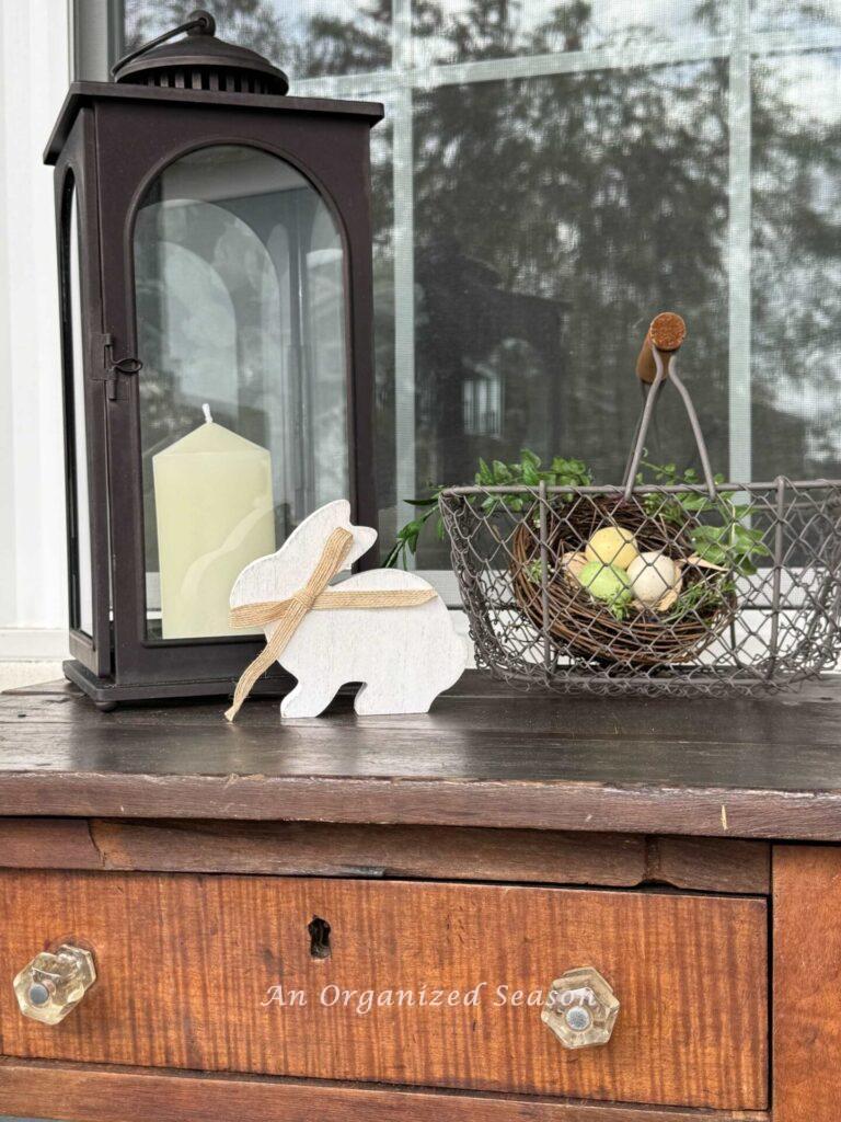 A lantern, wood bunny, and a chicken wire basket with a bird's nest inside. 