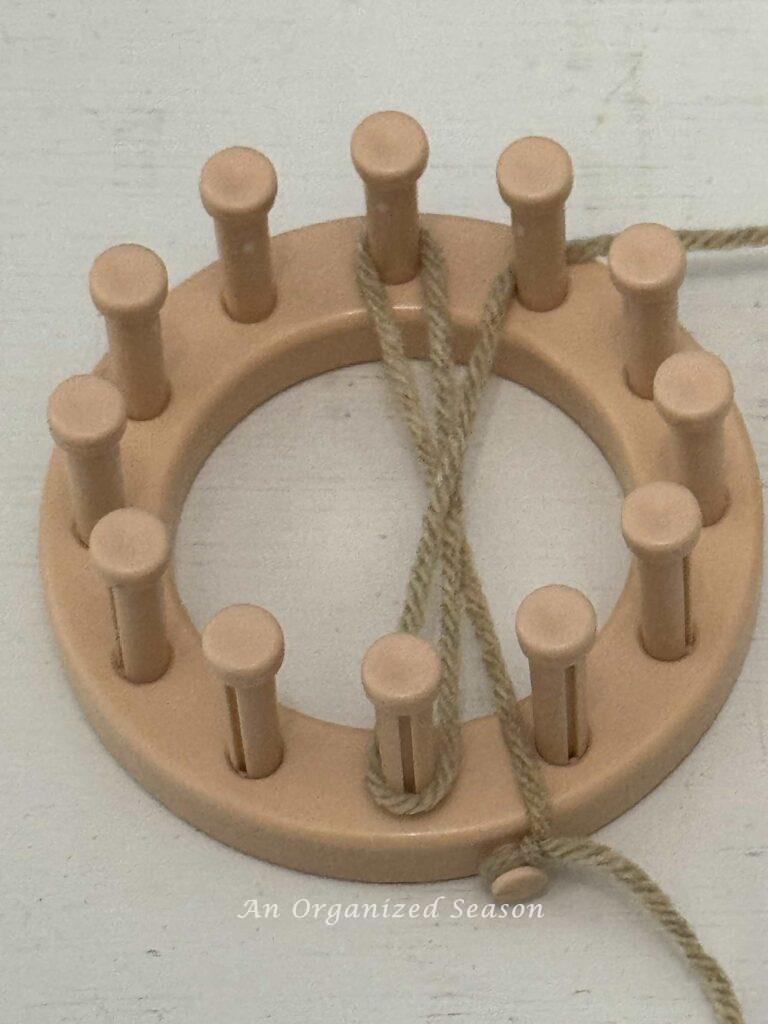 A round loom with tan yarn wrapped around two pegs. 