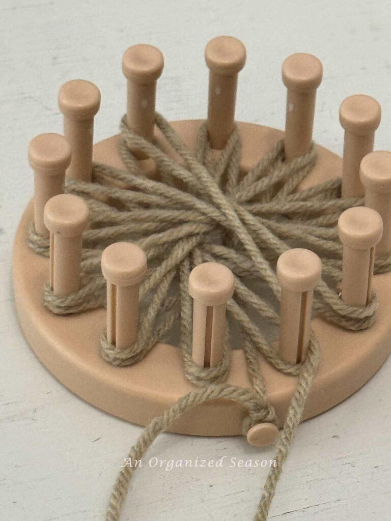 A round loom with two layers of tan yarn wrapped around all the pegs.