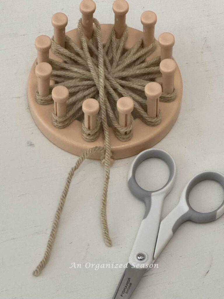 A round loom with three layers of tan yarn wrapped around all the pegs. 