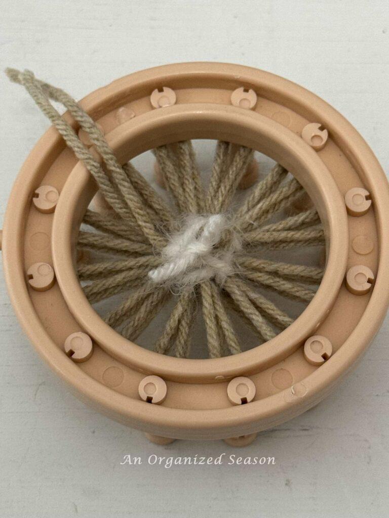 White yarn cut and knotted on the back of a round loom.