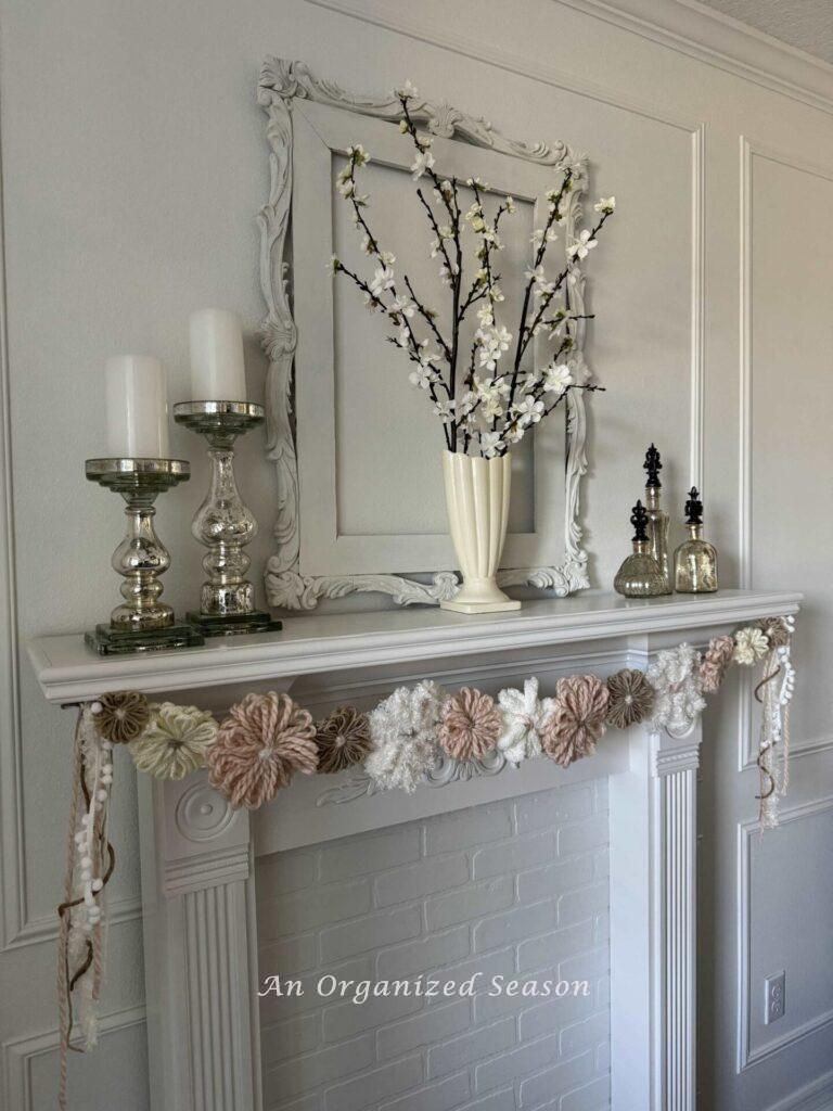 DIY yarn flower garland hanging on a white fireplace mantel.