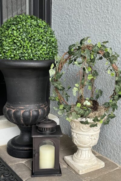 Two topiaries and a lantern on a porch.