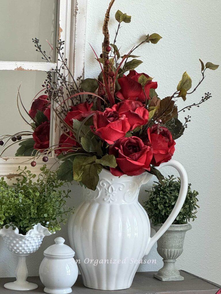 A white pitcher with an arrangement of red roses. 