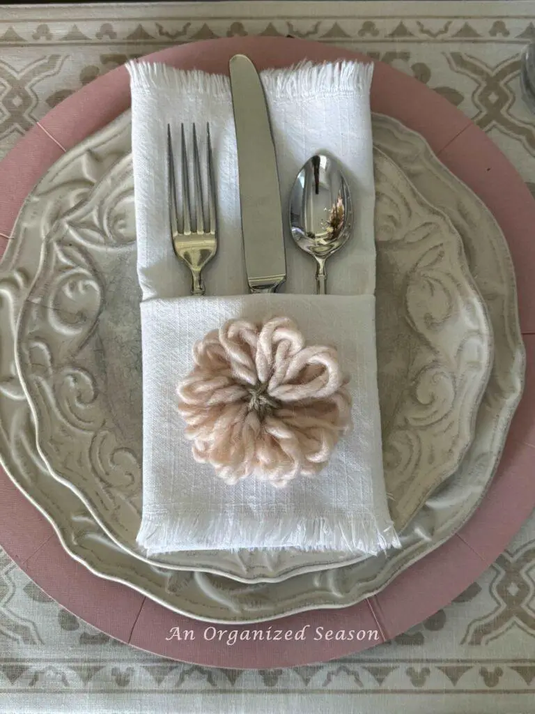 Mother's Day table decor idea four is to add a special touch like this napkin folded into a pocket with a yarn flower sitting on it. 