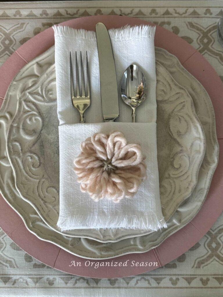 Mother's Day table decor idea four is to add a special touch like this napkin folded into a pocket with a yarn flower sitting on it.