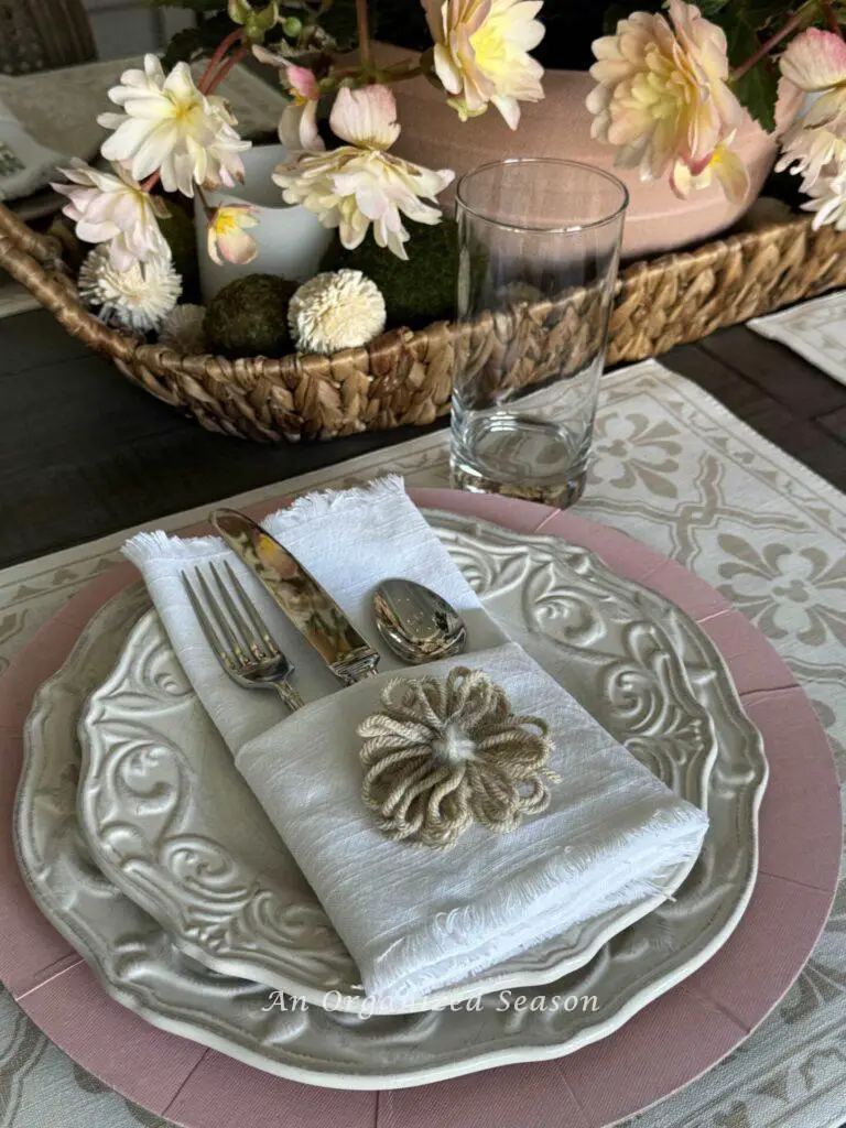 Mother's Day table decor idea three is to determine a place setting. This one uses a pink charger, beige plates, white pocket napkin, and a simple glass.  