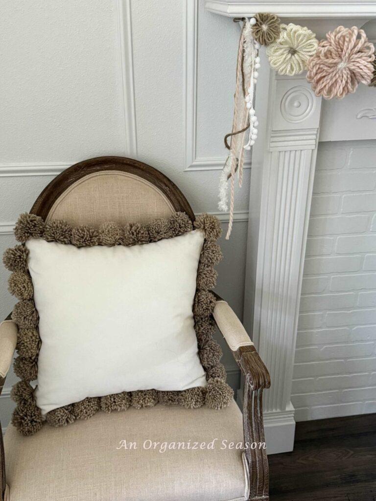 A pom pom pillow sitting in a chair. 