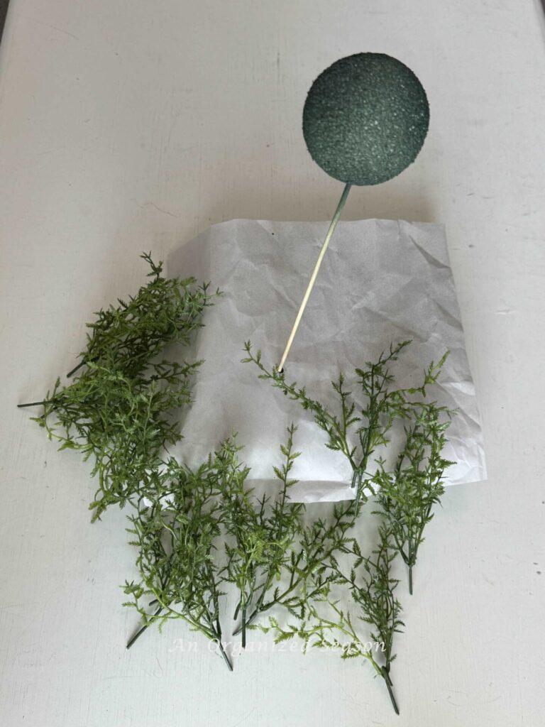 Step three to make a faux topiary is to cut stems off of a greenery pick.