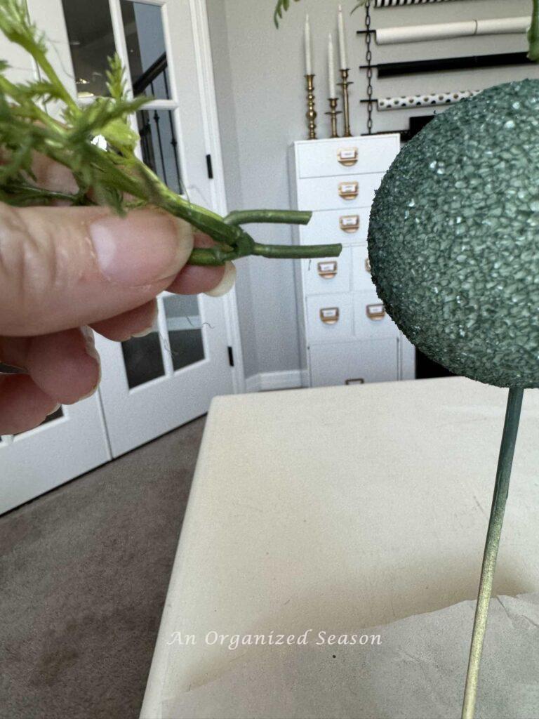 Step five to make a faux topiary is to insert the cut stem into the styrofoam ball. 