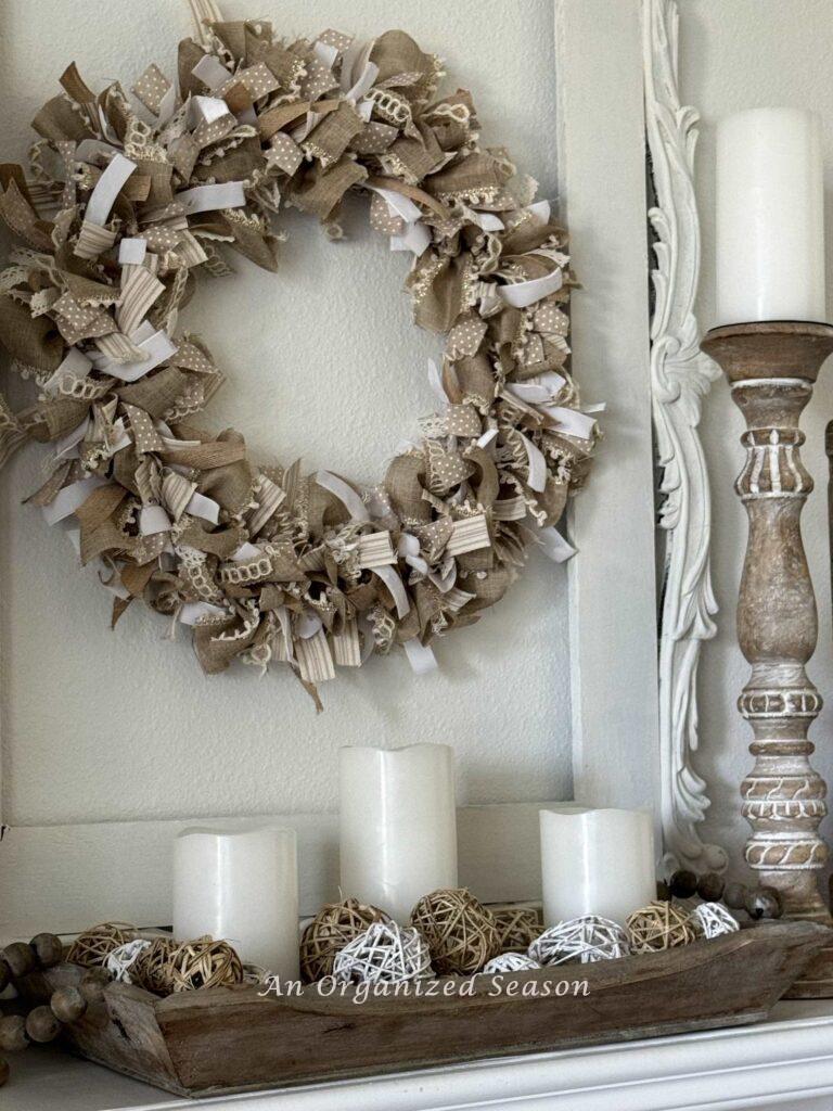 A neutral ribbon wreath hanging above a fireplace. 