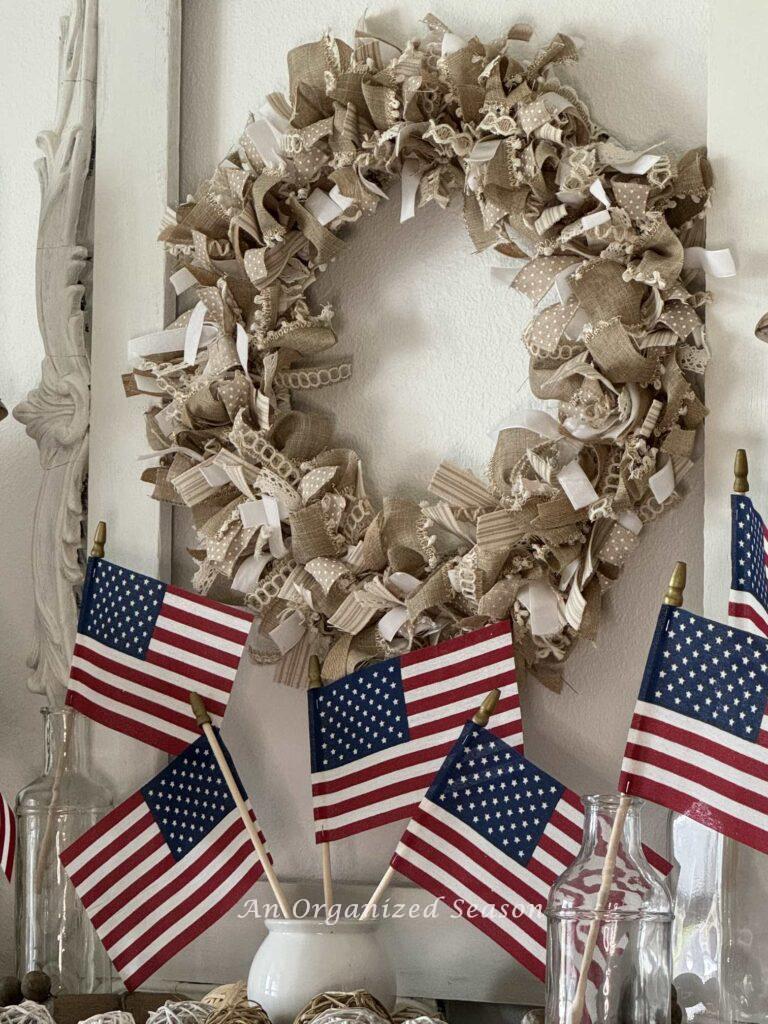 Flags in a white jar sitting on a fireplace.  with a neutral wreath above.