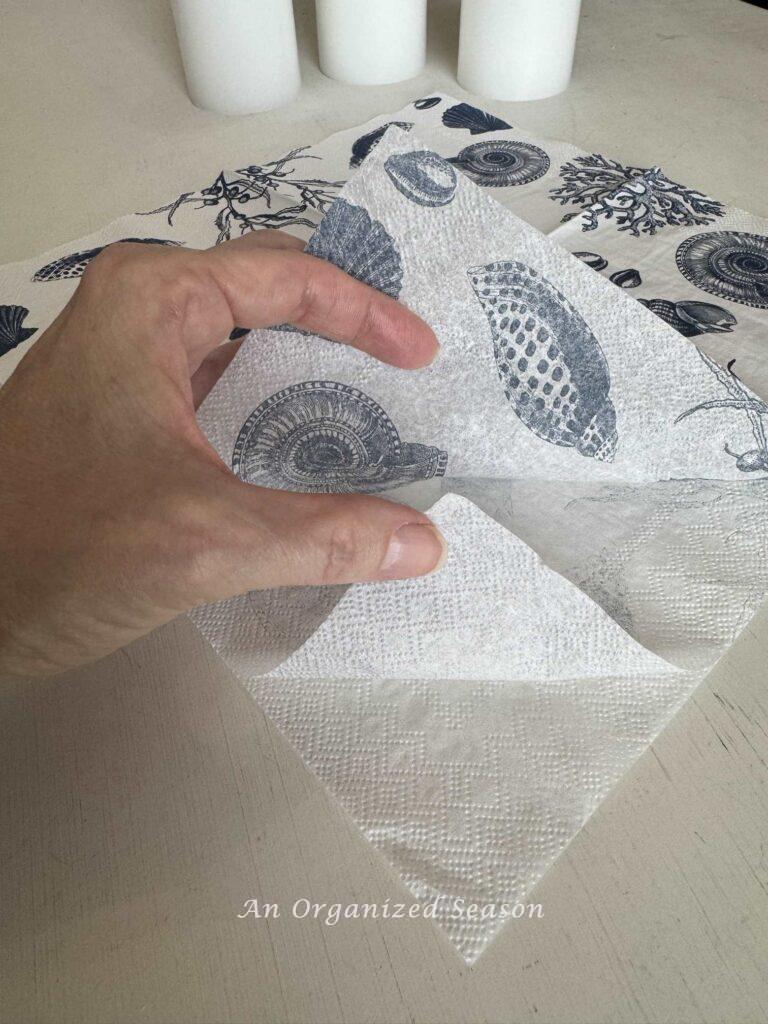Someone removing the white layers from the printed layer of a napkin.  