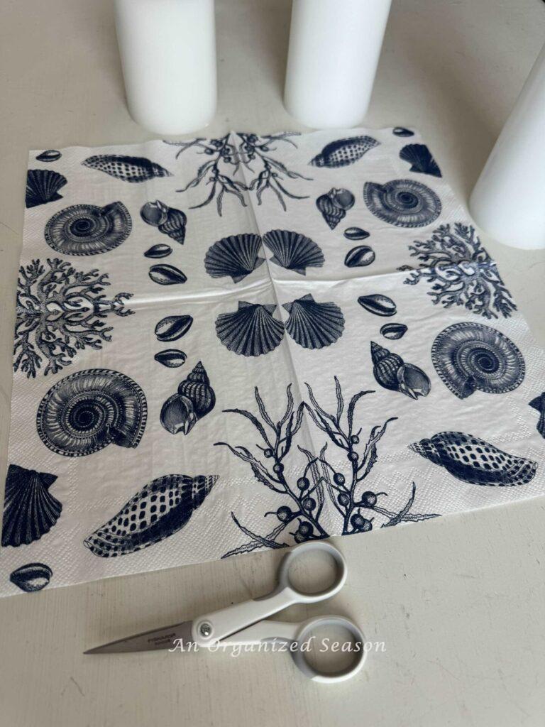 A napkin with shells on it and a pair of scissors.
