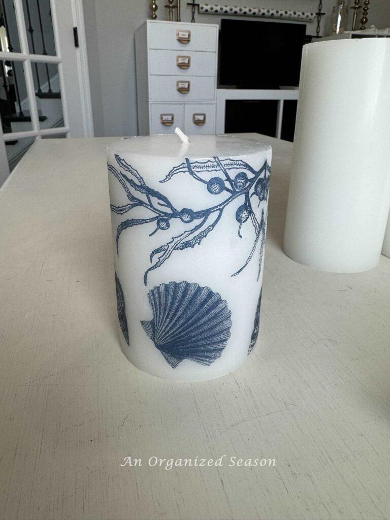 A white candle with blue shells on it. 