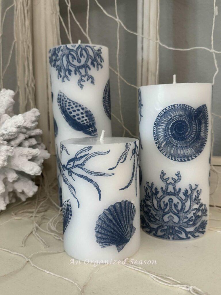 Three white pillar candles covered in blue shells. 