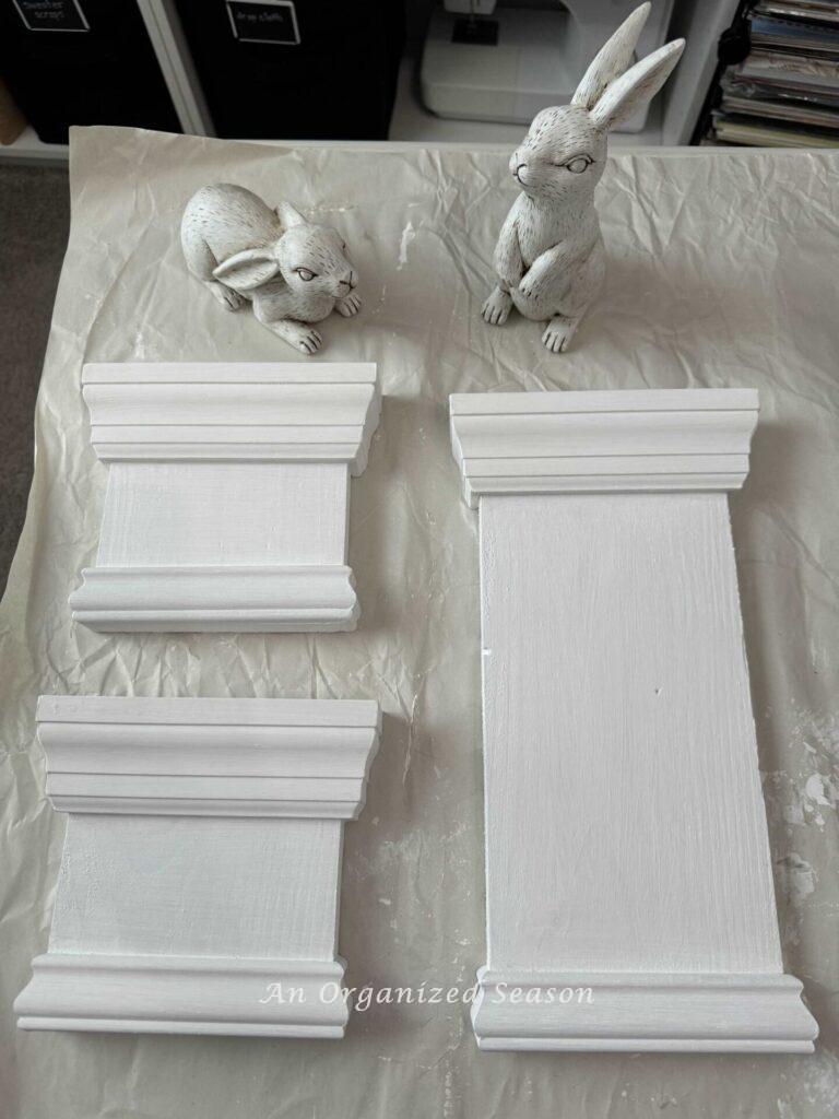 Three white wood bases and two white bunny statues. 
