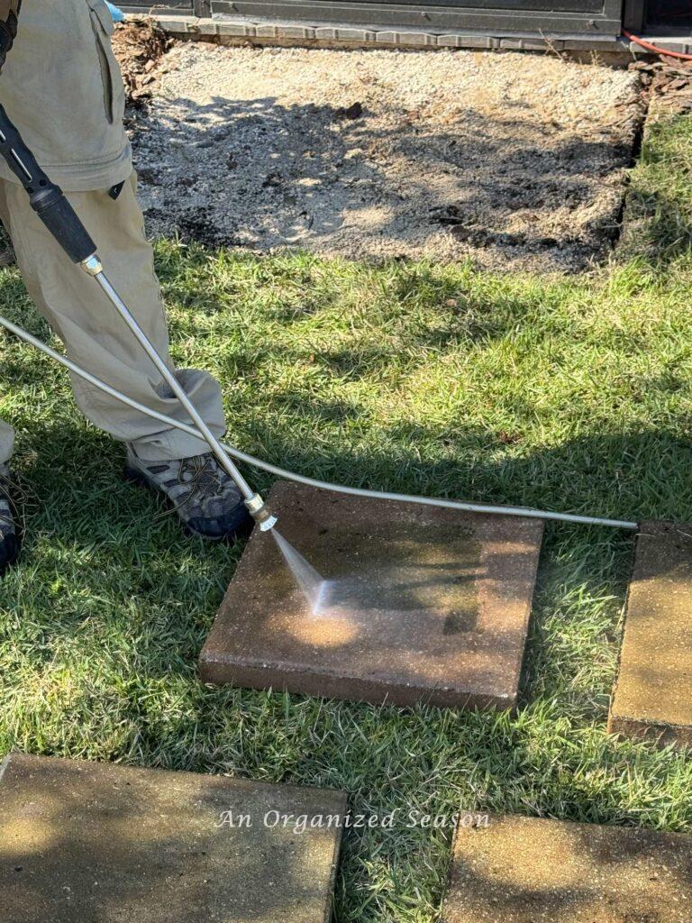 A man performing DIY lawn care by power washing pavers. 
