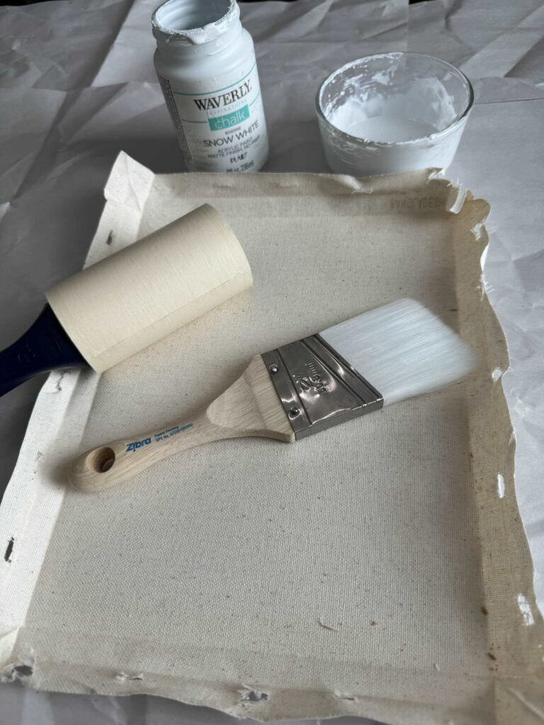 Step two to make DIY seashell wall decor is to clean the canvas with a lint roller and paint it with white chalk paint and a brush.  