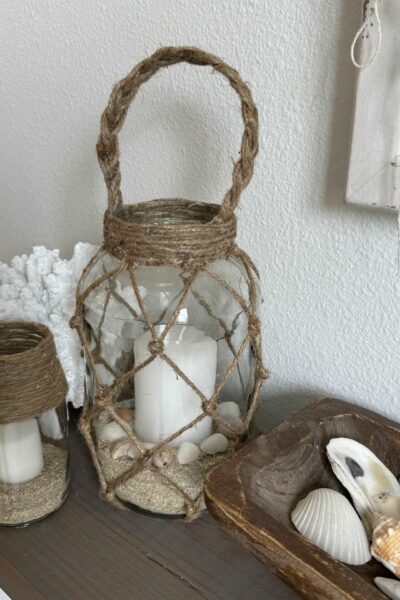 A coastal lantern, glass candle holder, and a piece of white coral.