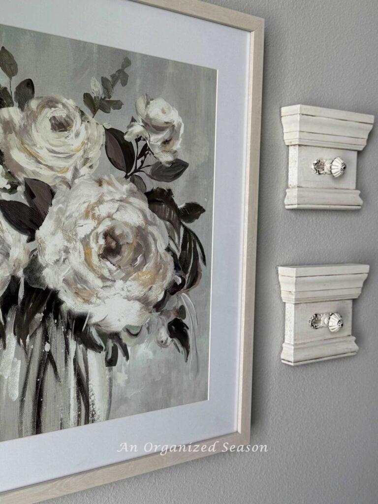Two DIY wall hooks hanging next to a floral picture. 