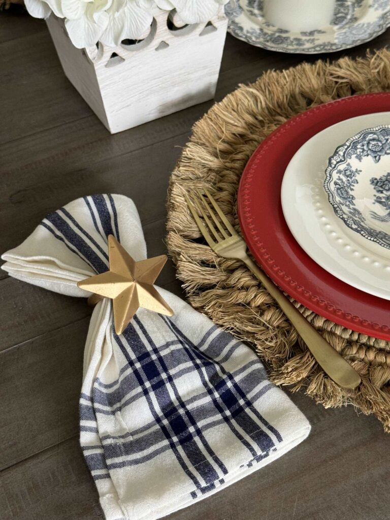 A blue and white napkin with a gold star ring, a gold fork and set of red, white, and blue plates. 