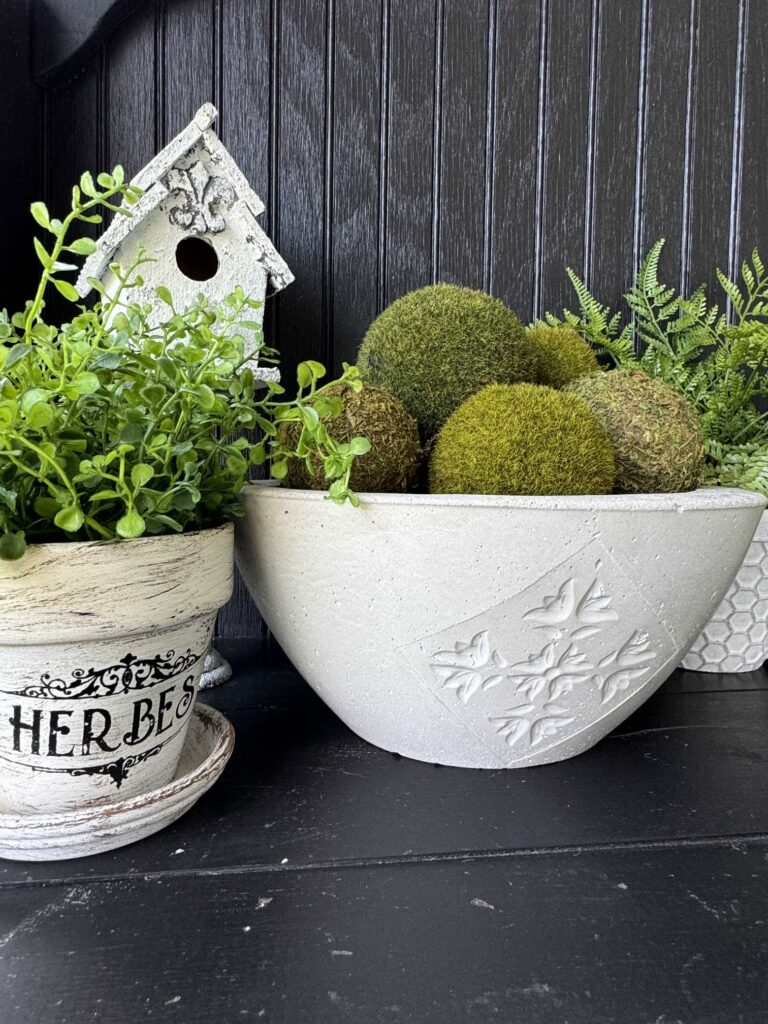 Concrete bowl next to a pot of herbs and a birdhouse. 