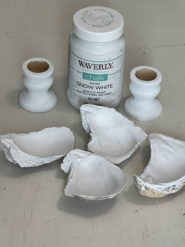 Two wood candleholders and four oyster shells painted white.