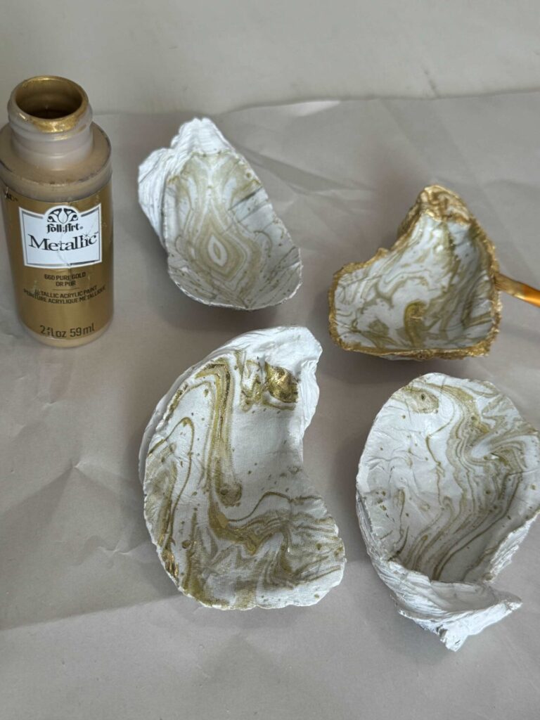 Someone painting a gold edge around a decoupaged oyster shell. 