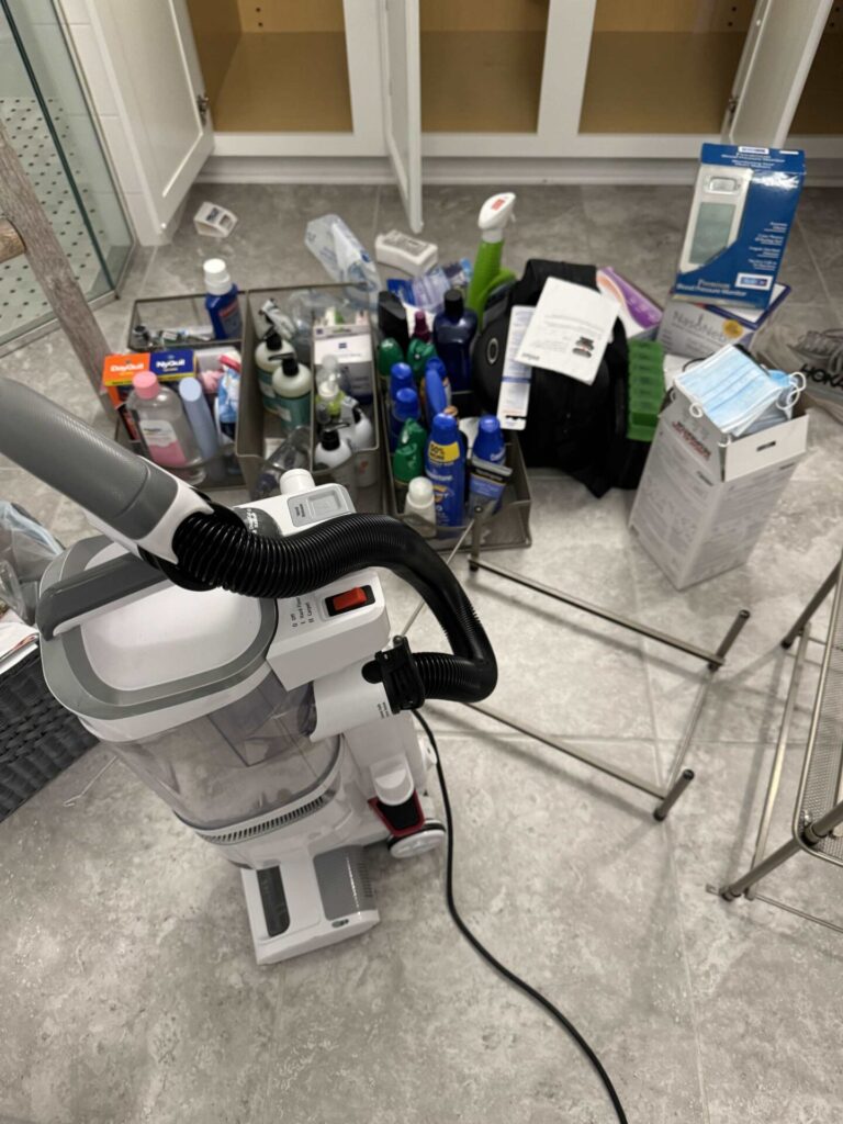 A cleaned out bathroom cabinet with beauty products covering the floor. 