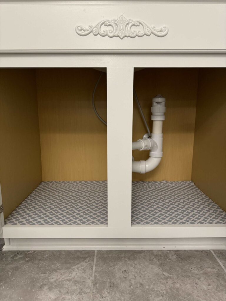 A clean cabinet under a bathroom sink with shelf liner in the bottom. 