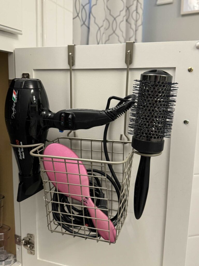 An over the door hair tool organizer hanging on a bathroom cabinet door. 