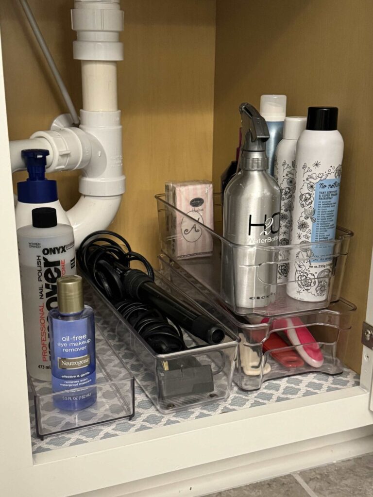 Plastic bins organize and contain beauty products under a bathroom sink.  