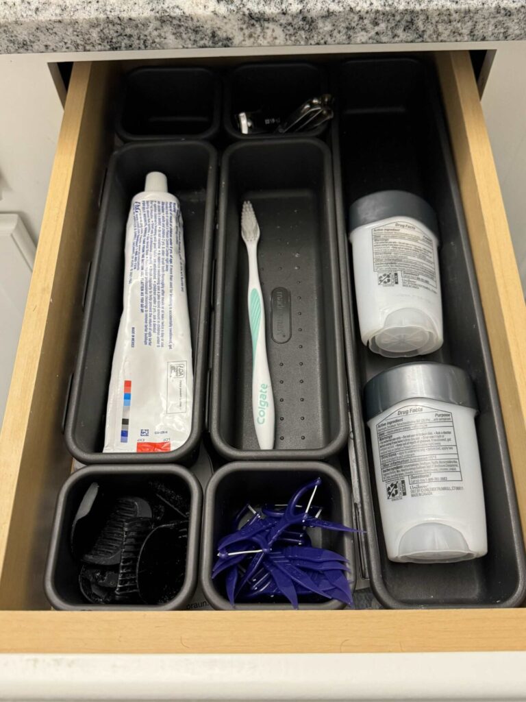 Black bathroom drawer organizer bins filled with toiletry items.