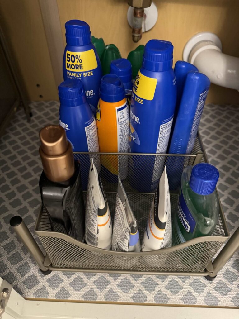 Sun care items organized in a mesh wire drawer in a bathroom cabinet. 